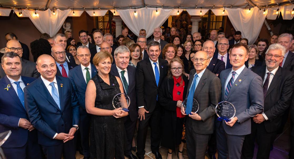 A large group of people, three of whom are holding crystal awards.