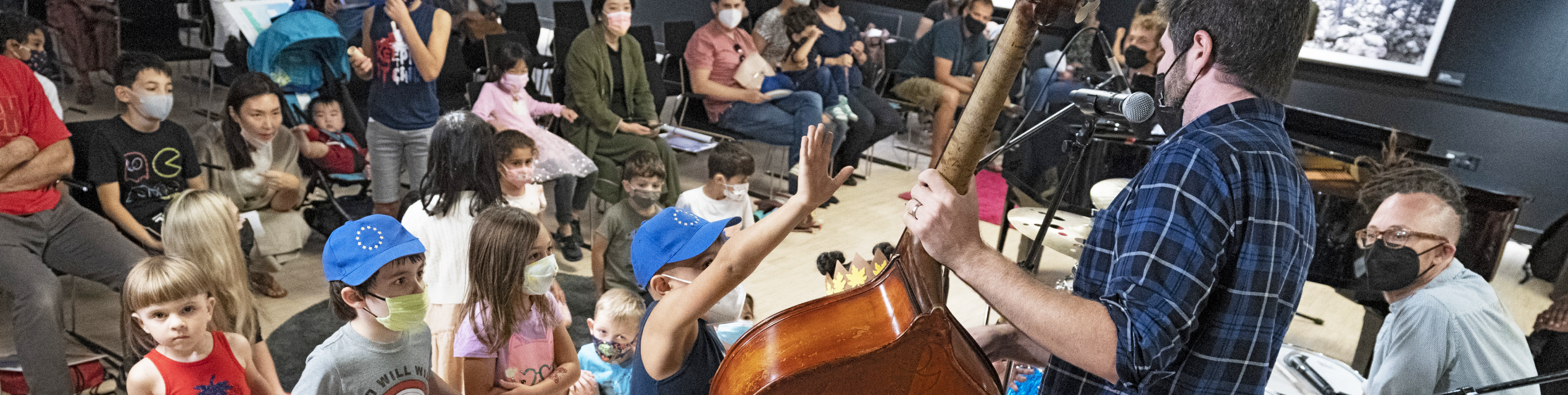 A man plays the cello in front of young children wearing masks.