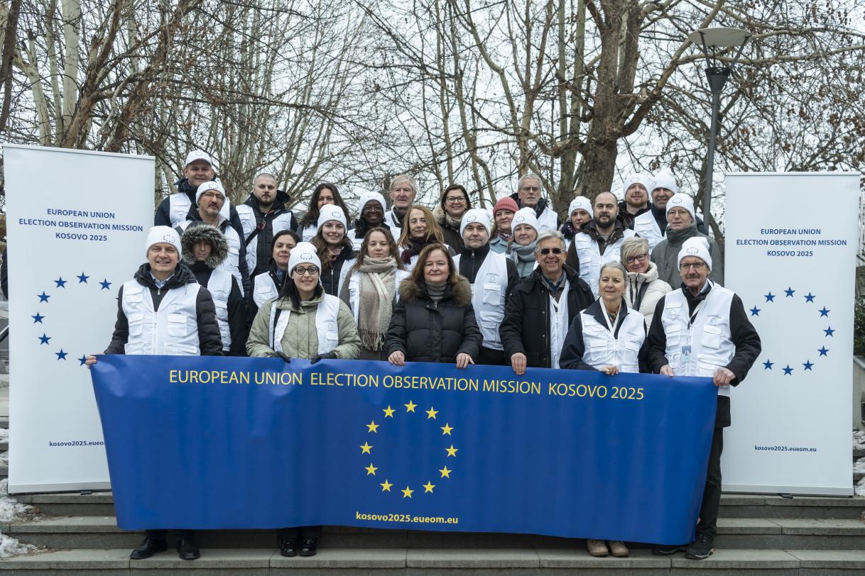 Observers standing behind the mission banner