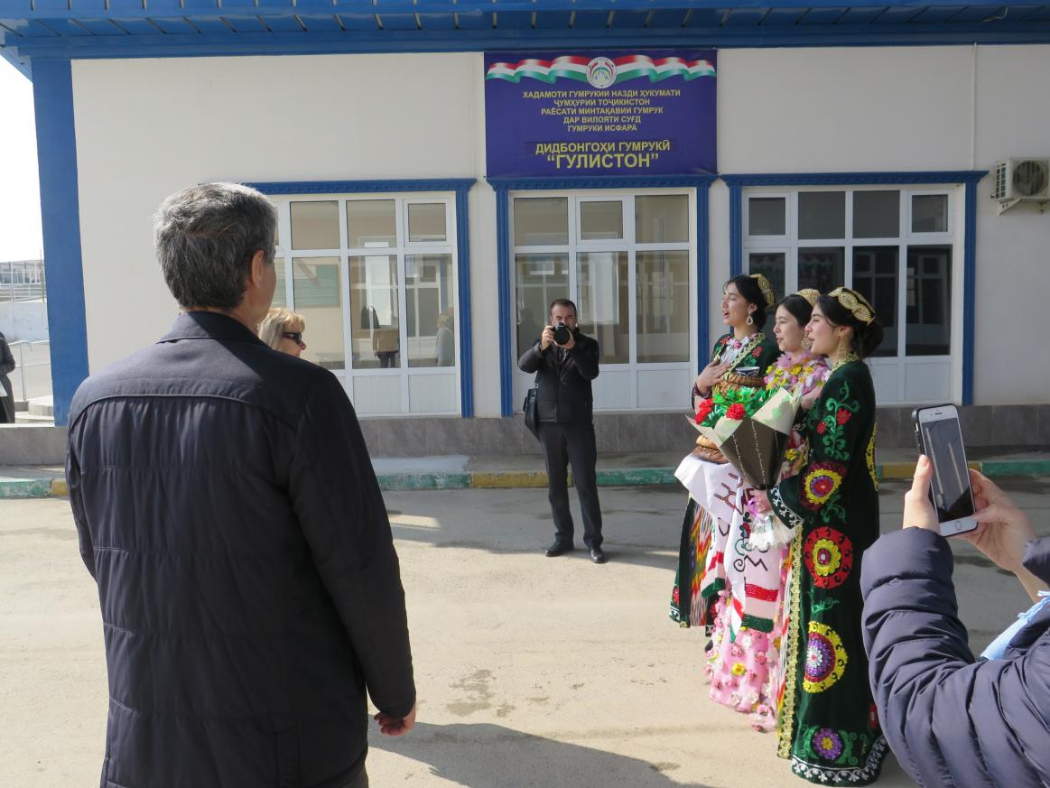 Three people in traditional costumes singing, two people taking pictures.