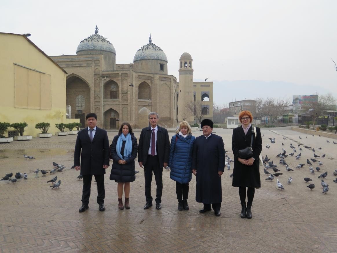 A group of six people posing for the camera in front of a mosque. A lot of pigeon in the ground.