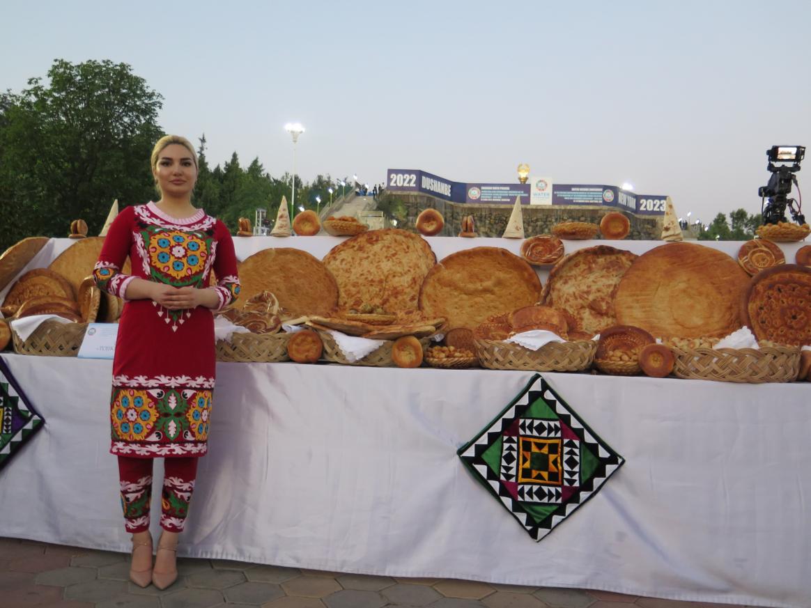 A person in a colourful dress posing or the camera in front of a table with large round breads.