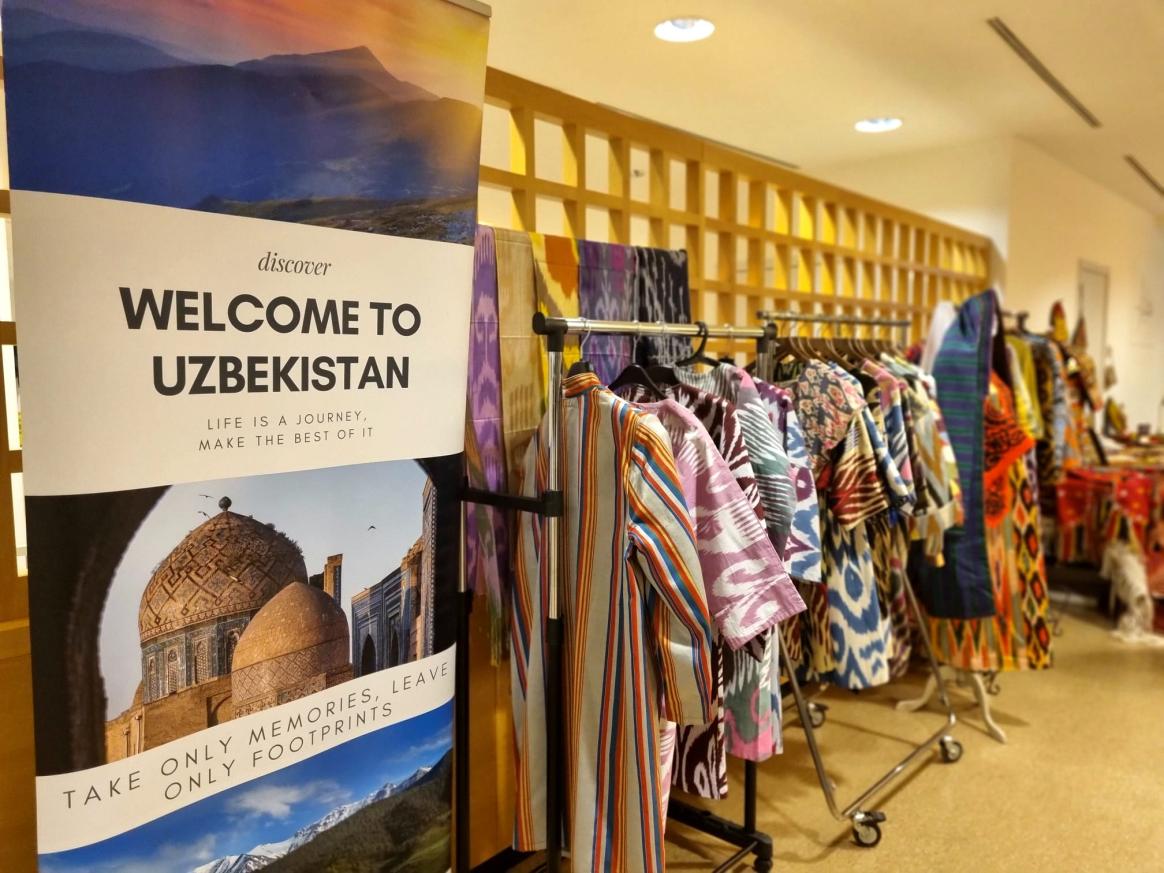 Banner that says 'Welcome to Uzbekistan' with rack of clothes behind