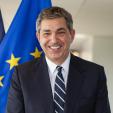 Ambassador Lambrinidis stands in front of one EU and one EU flag.