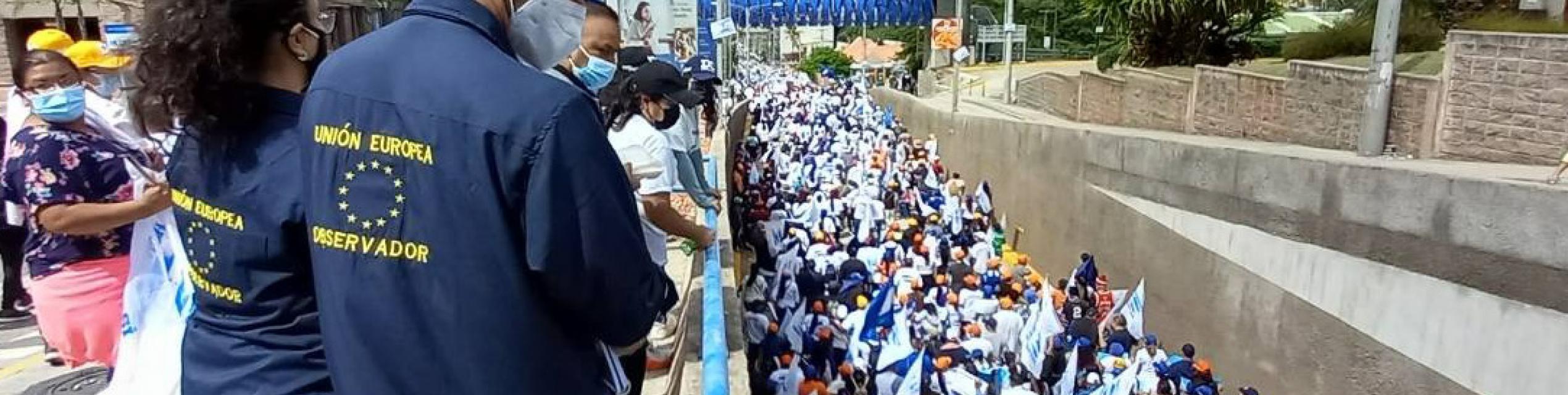 people marching with flags and EOM observers watching them
