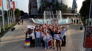 Group of people cheering and standing on a square in front of a fountain