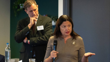 A speaker in foreground with the chairperson in background listening closely.