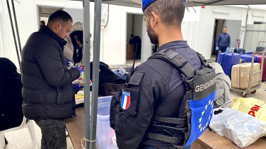 EU officer observing baggage screening at a checkpoint.