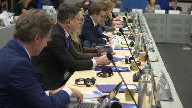 Picture of participants of the EU Communication Directors' Meeting, where a row of participant is seen sitting at a table, whilst listening to a speaker in the background