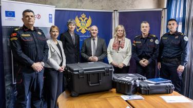 Liselotte Isaksson, Ekaterina Paniklova, and representatives of the border police standing in front of a table. The donated equipment is on the table. 