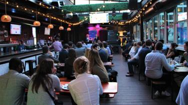 A large rooftop bar filled with people drinking and listening.