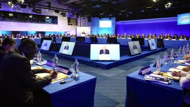 A VIP addresses a forum while appearing on several screens.