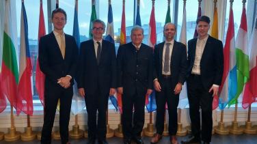 Picture of 5 men in suits in front of flags