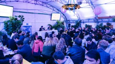 A large crowd gathers underneath a white tent while Ambassador Lambrinidis speaks into a mic upfront.