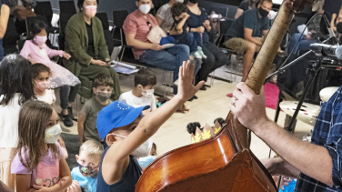 A man plays the cello in front of young children wearing masks.