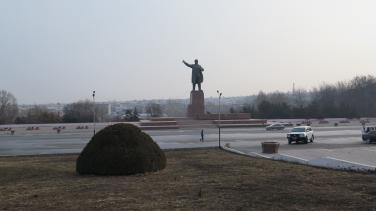 Large statue next to a road with few cars and one pedestrian.