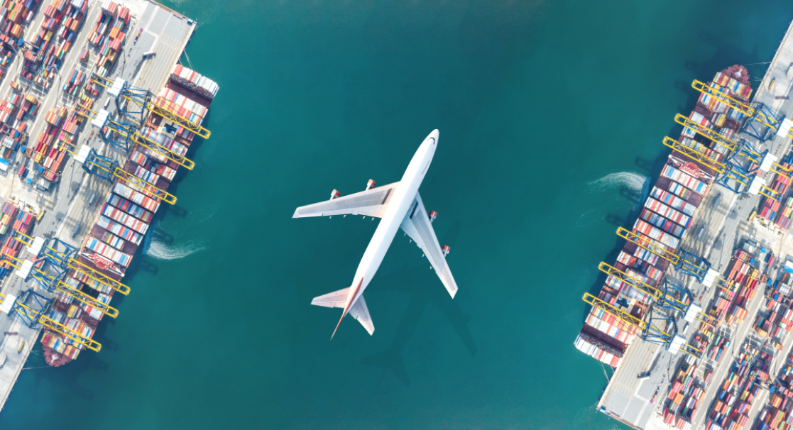 Overhead view of a passenger aircraft overflying a container terminal.
