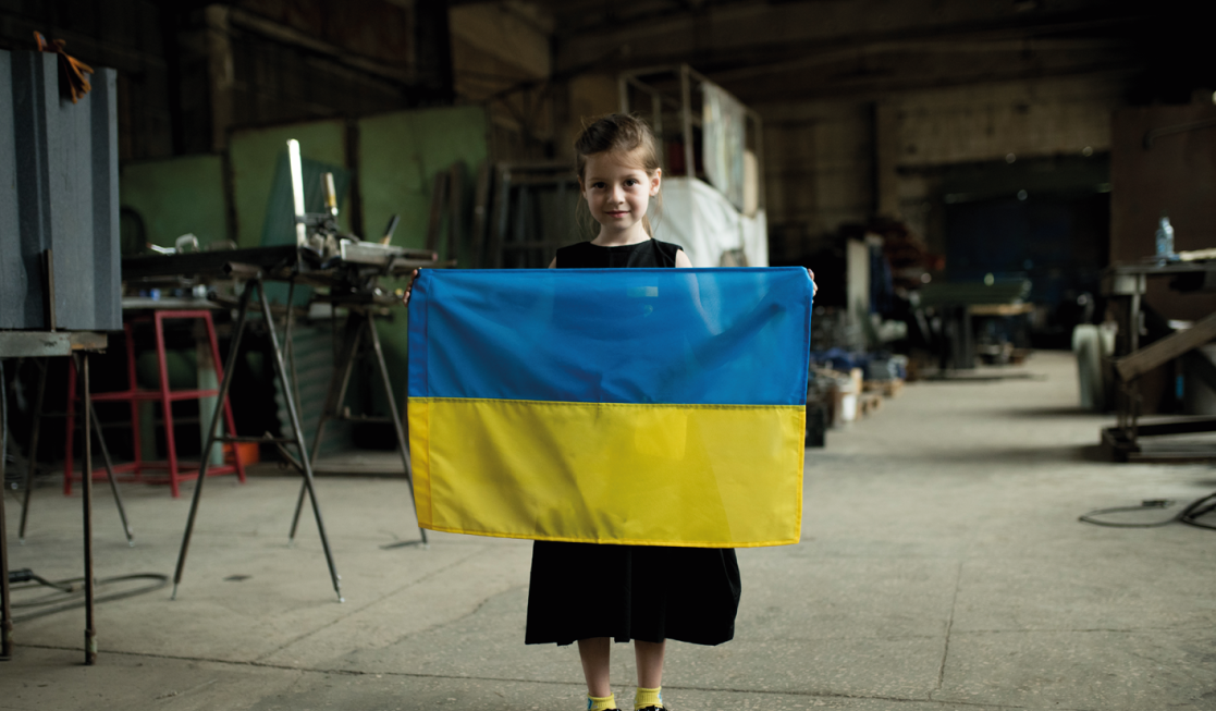 [photo: Ukrainian girl holding Ukrainian flag at the volunteer center] 