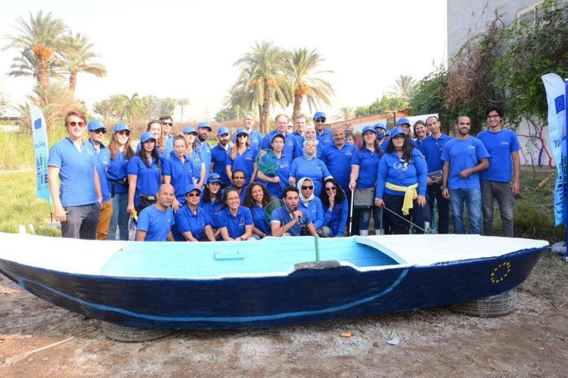 Group of people in blue T-shirts and caps posing behind a boat