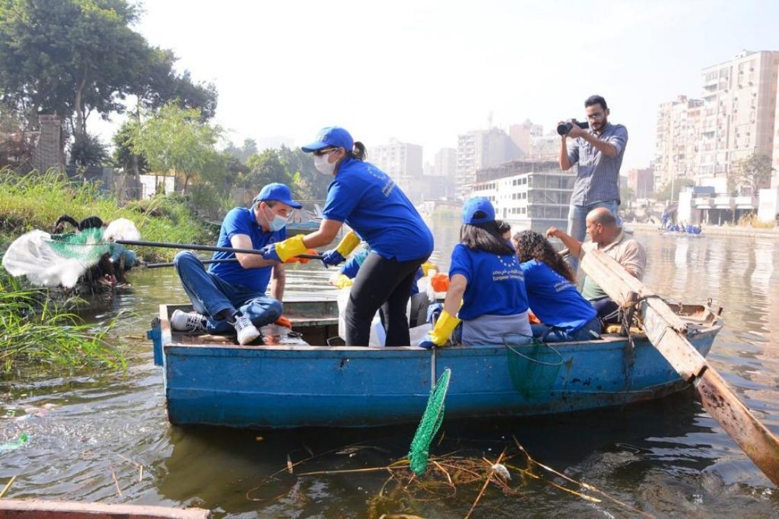 Group of people in blue T-shirts and caps on a boat collecting rubbish from the river