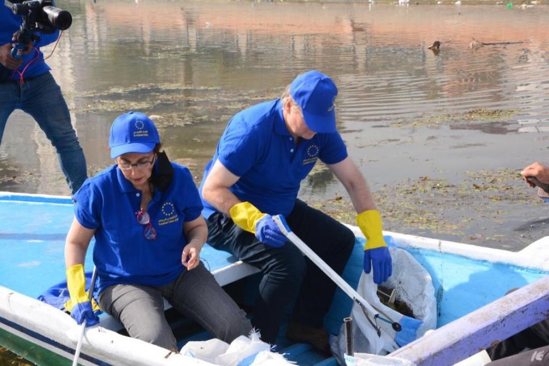 Two people in blue T-shirts and caps on a boat collecting rubbish from the river