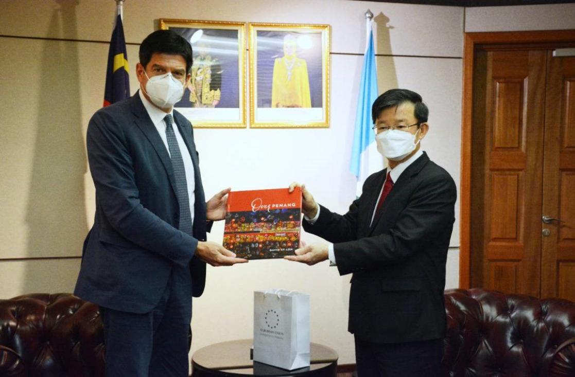 Two men holding a book in an office in front of two flags