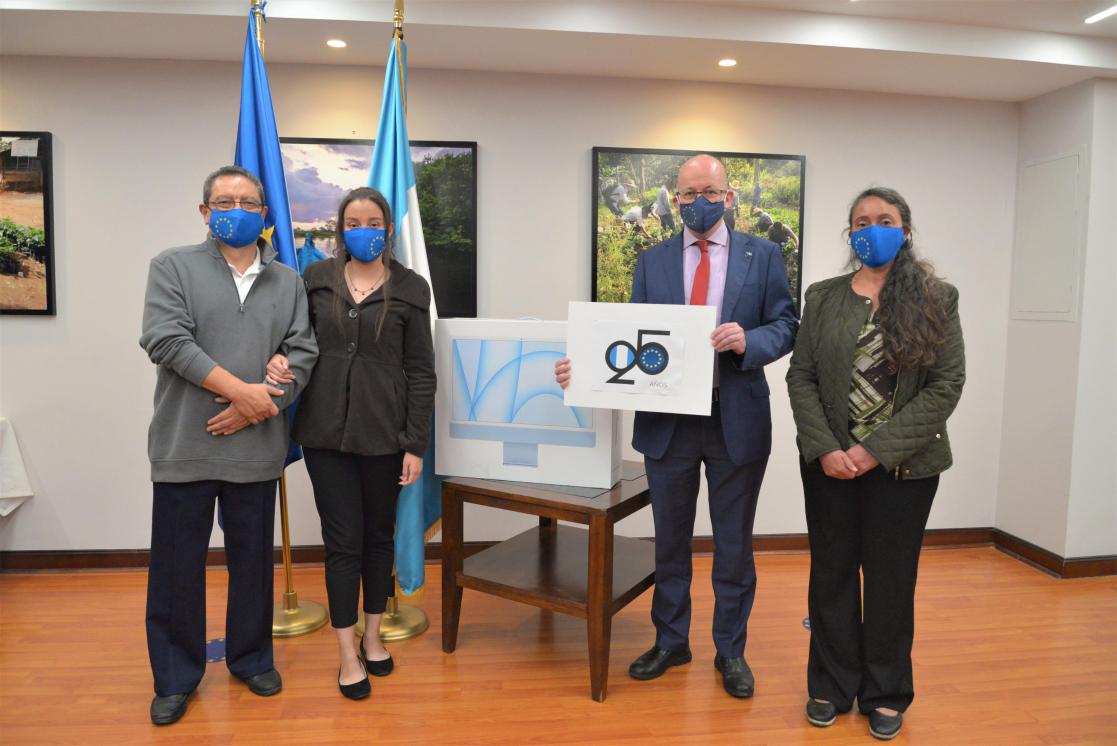 Four people posing with the flag of the European Union and another blue and white flag