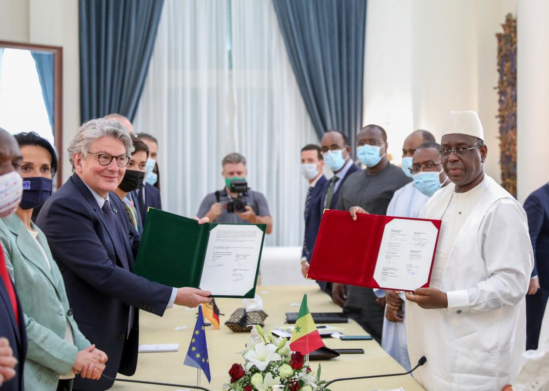 Two men posing with red and green folders during a meeting with other people