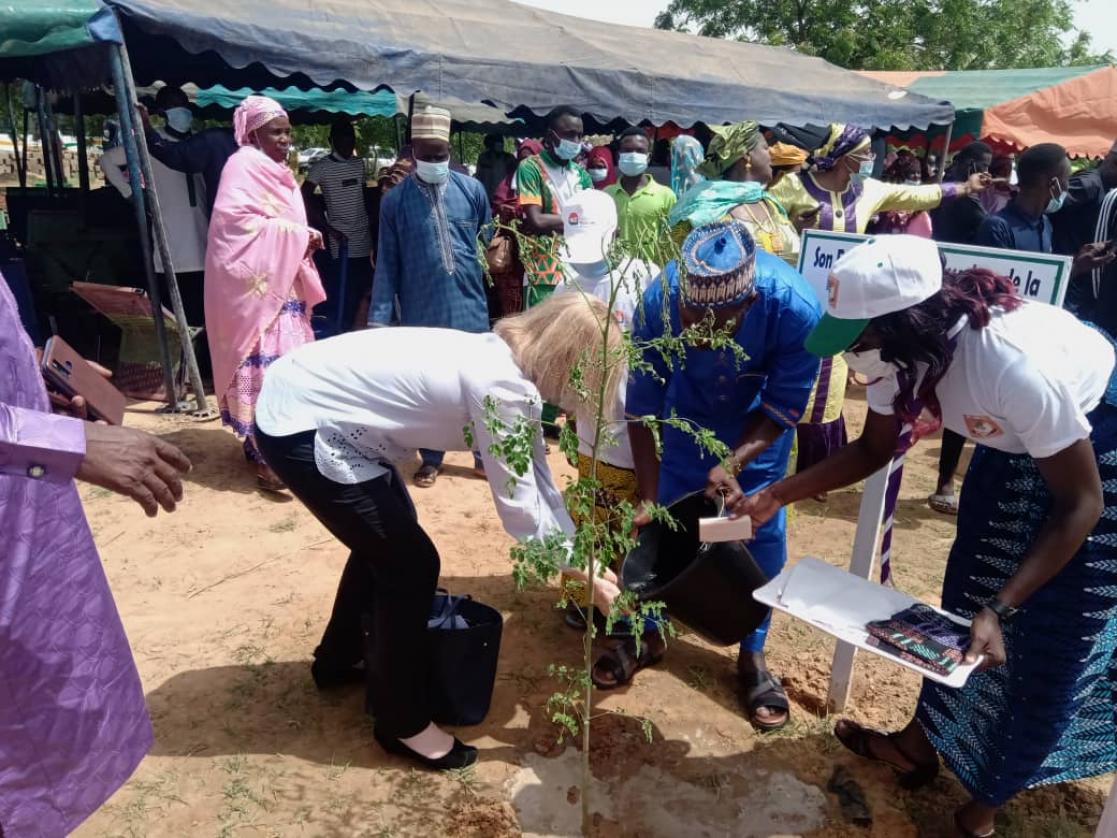 Woman washing her hands with a bucket held by a man surrounded by people during an event