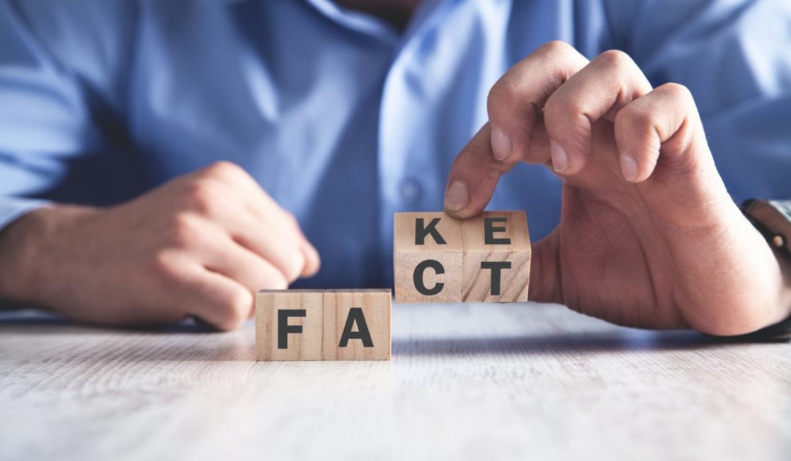 Hands placing wooden cubes with the word "fake".