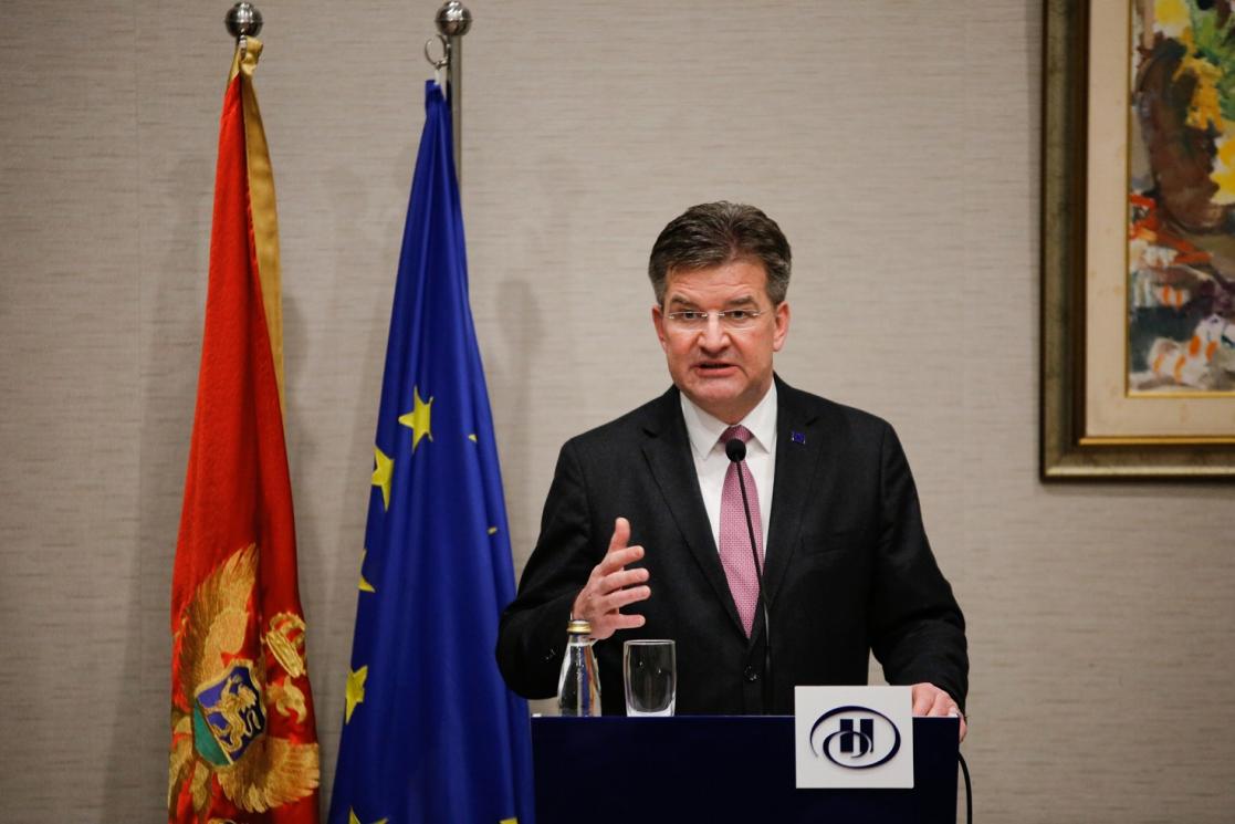 Man talking to an audience with flags on the background