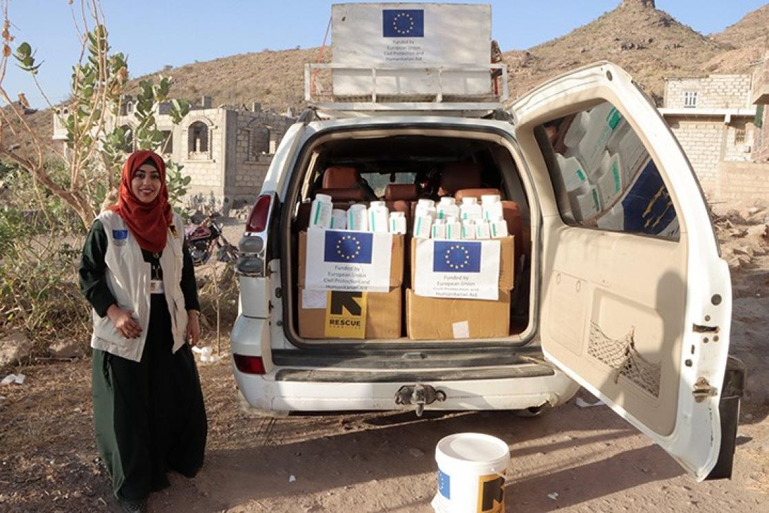 Woman posing next to a car with an open boot full of boxes and cans