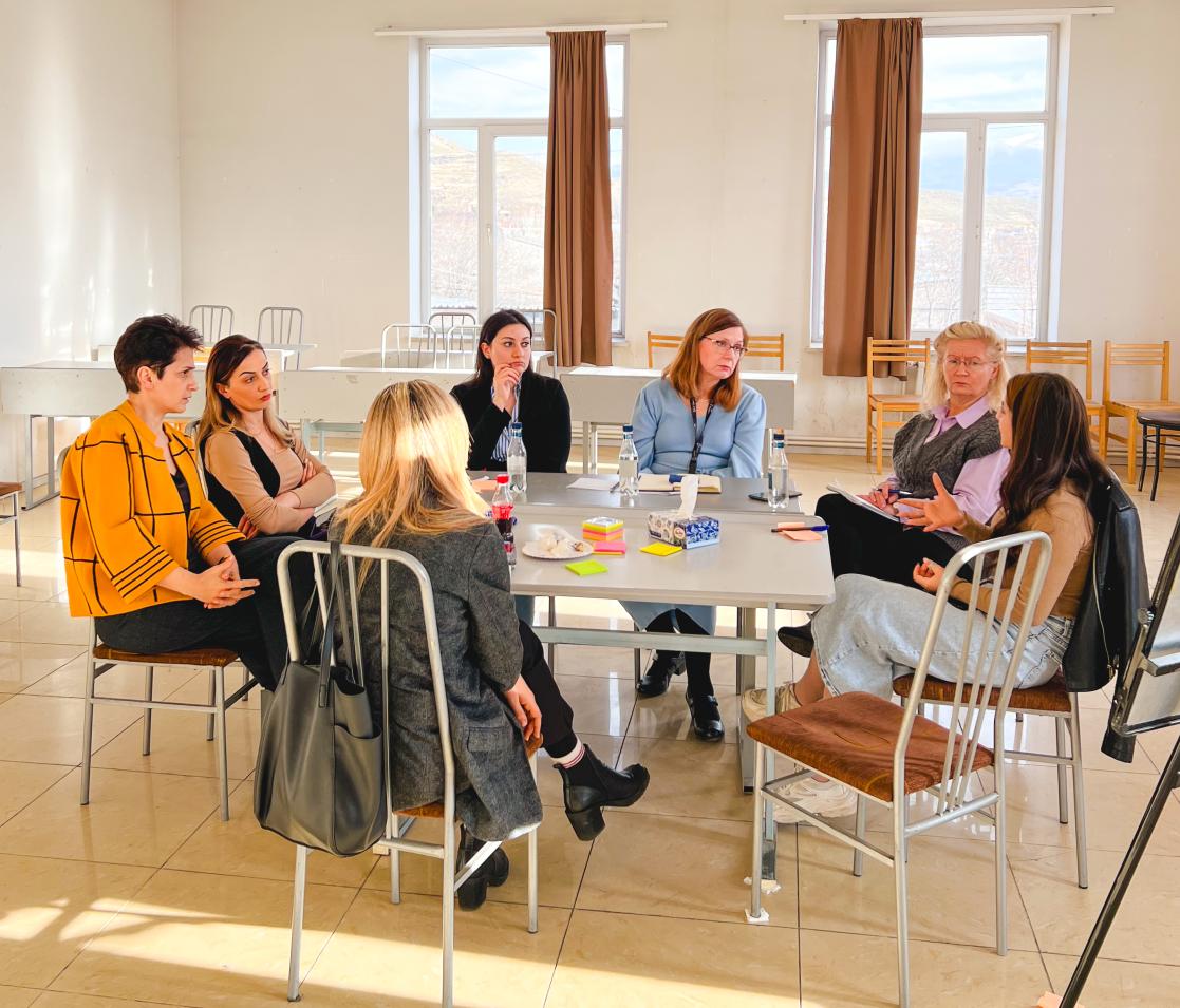 A group of seven people sit around a table in discussion at a seminar.
