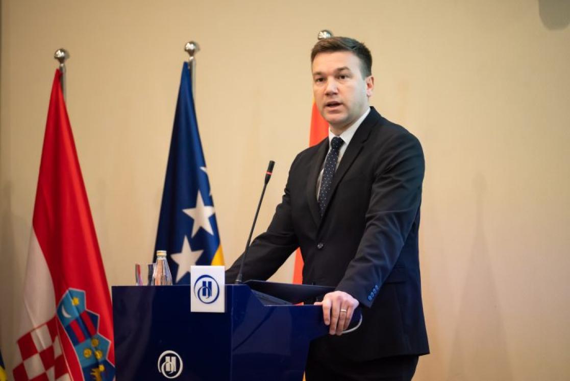 Domagoj Mikulić, State Secretary at the Ministry of reginal development and EU funds of the republic of Croatia , standing. Left of him there are twso flags Cratian and the flag of Bosnia and Herzegovina