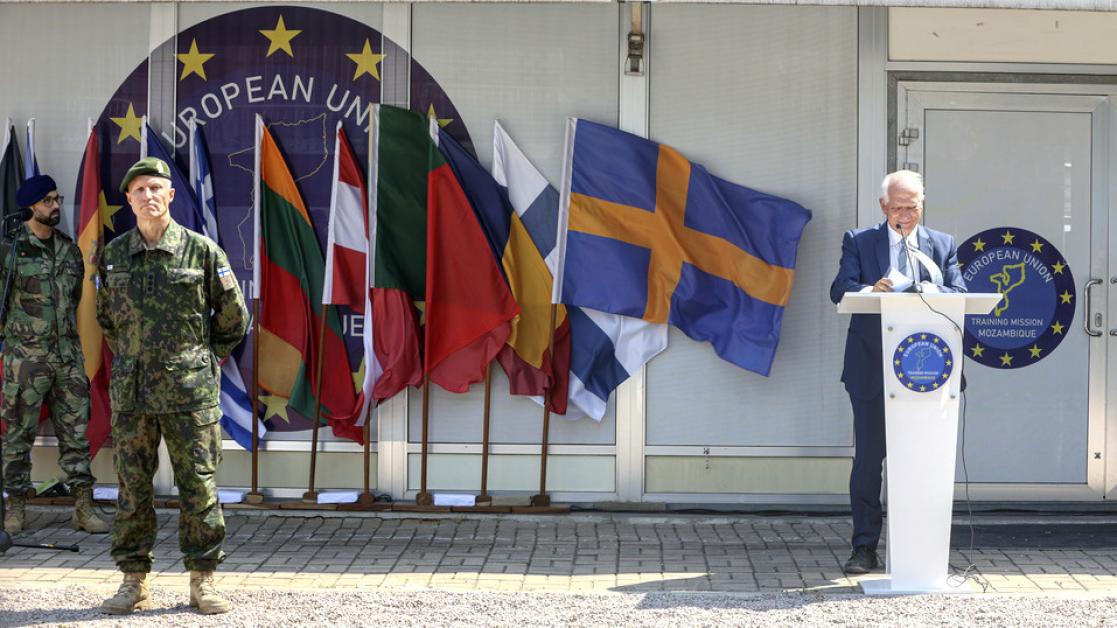 A man speaks at a military ceremony staged before many national flags. 