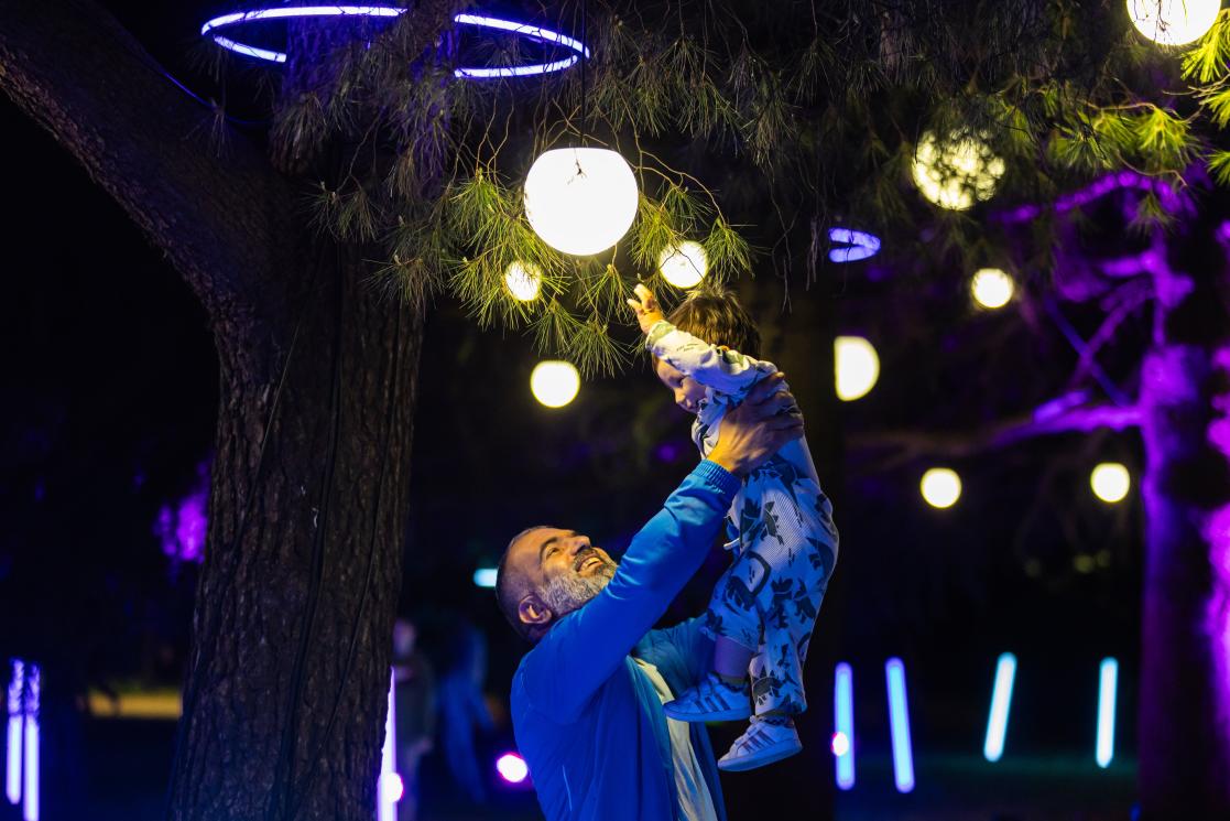 Man holding a child in the air beneath a tree decorated with lampions 