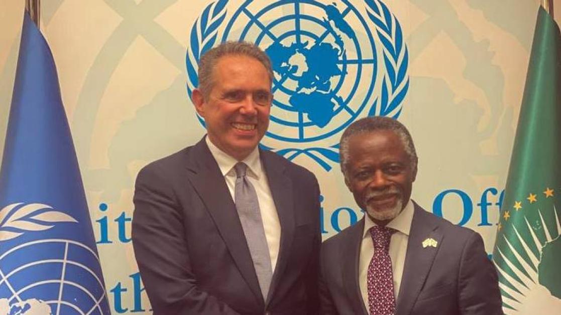 Two high level diplomats pose in front of a UN banner.