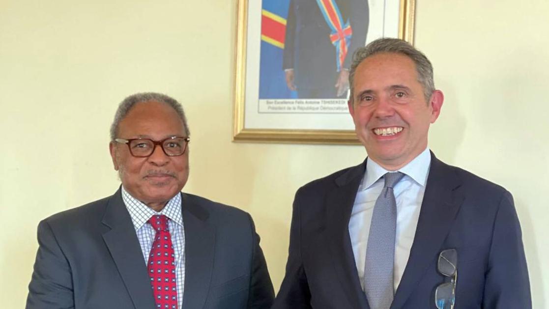 Two officials pose with a portrait photo on the wall in the background.