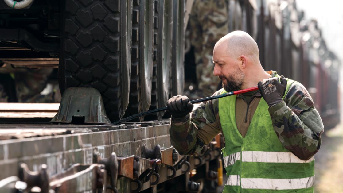 Trooper loading a train transport with military vehicles.