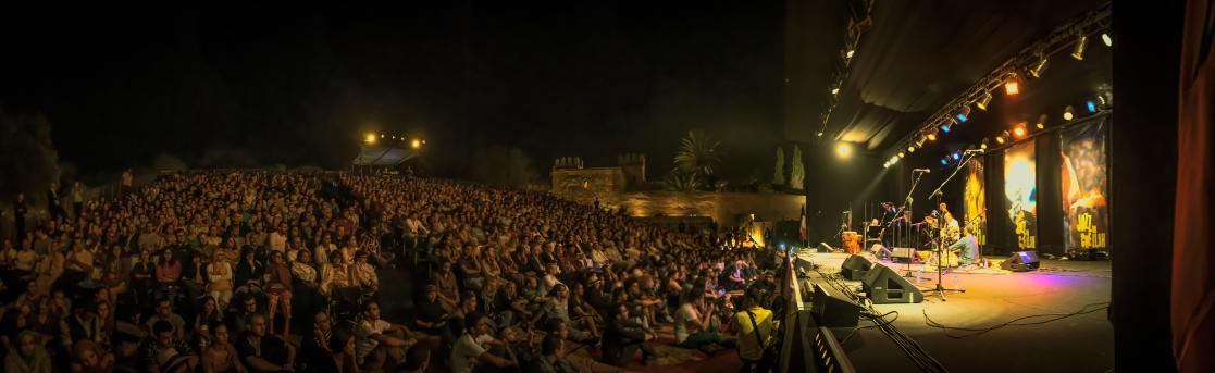 des gens assis sur des gradins et par terre devant une scène de festival de musique