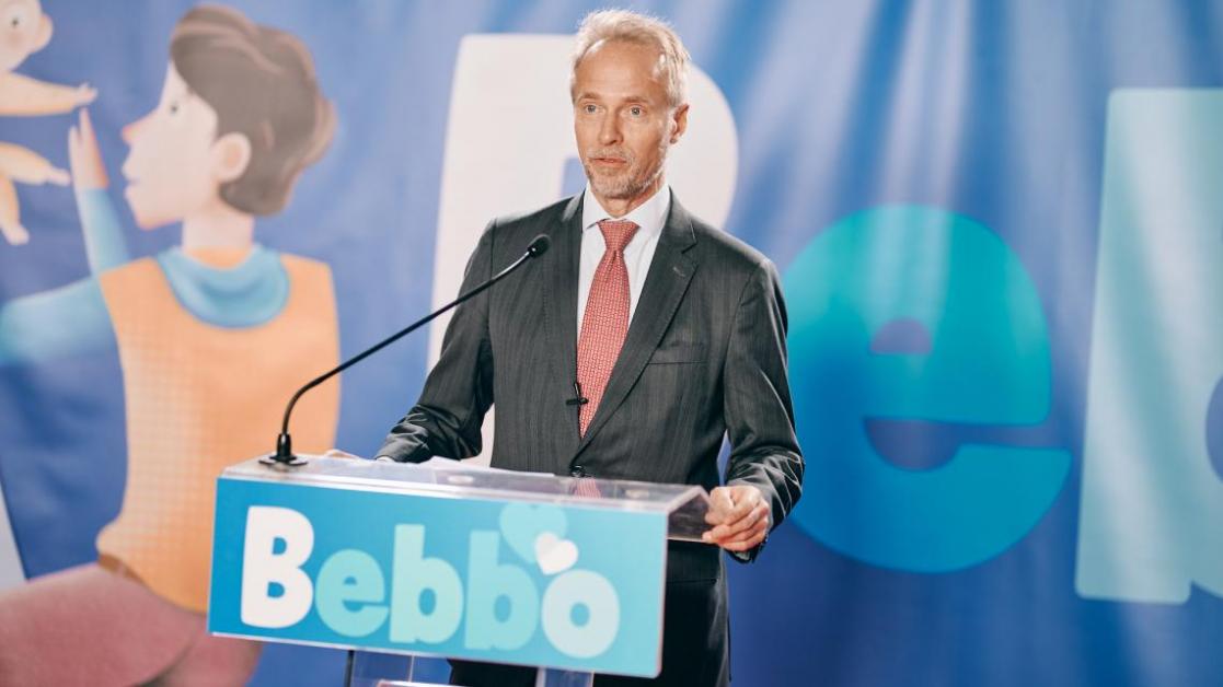 Man speaking at a lectern with the Bebbo advertising sign