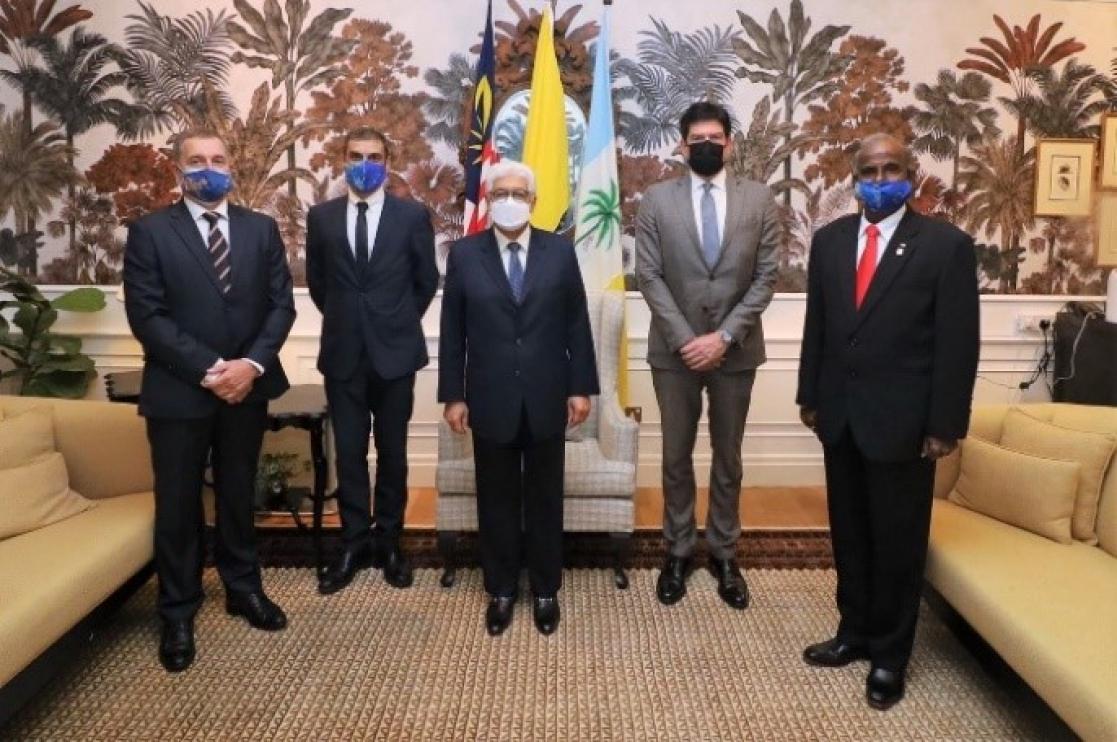 Five men posing in a hall in front of three flags