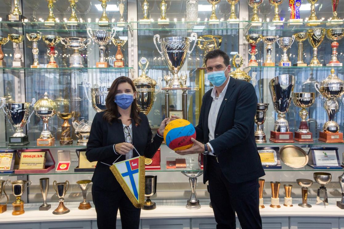 Man and woman holding a signed ball and a pennant in front of shelves full of trophies