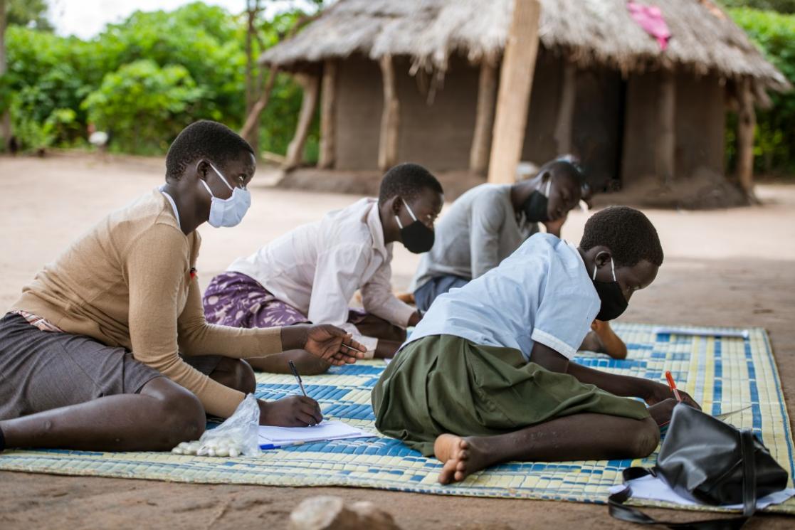 Children writing on papers sitting on the ground