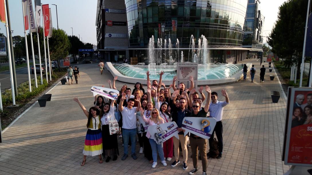 Group of people cheering and standing on a square in front of a fountain