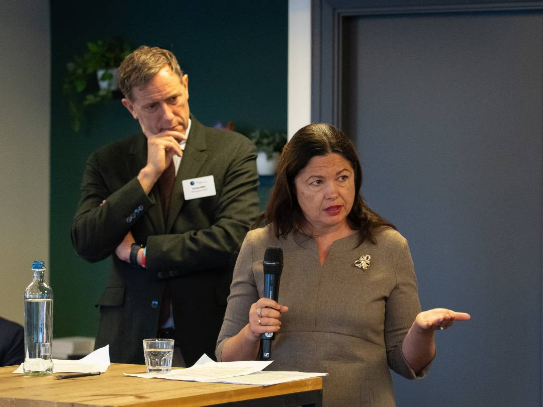 A speaker in foreground with the chairperson in background listening closely.