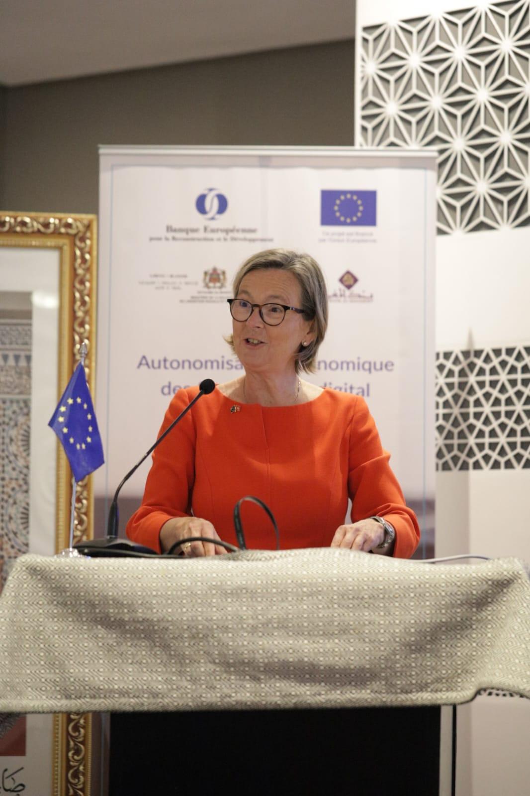 Une dame habillée en orange derrière un pupitre prononçant un discours