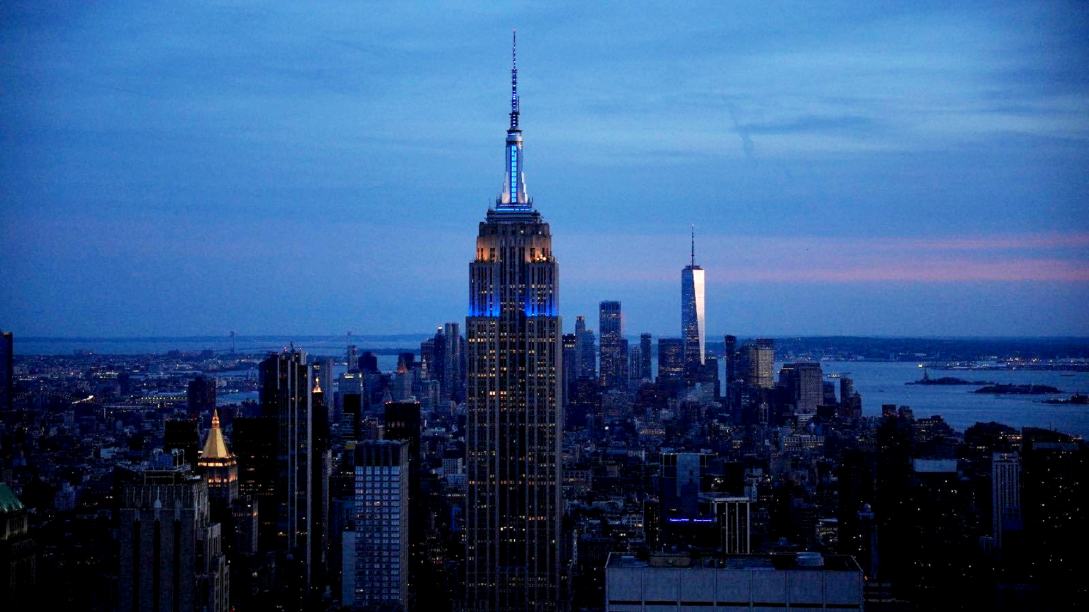 The Empire State Building in New York City glows blue and yellow.