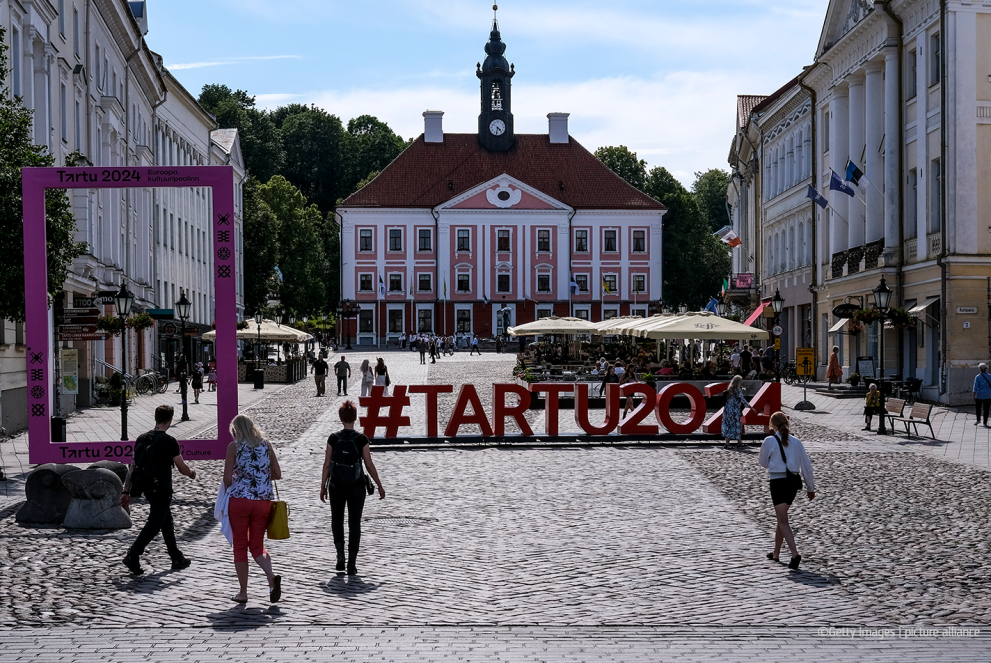 Tartu city square. People are walking across it and there is a sign #tartu2024 on the ground