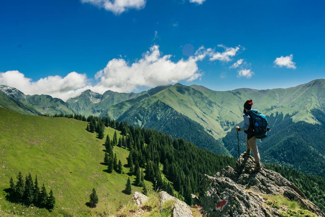 Man standing on a cliff and surrounded by green mountains